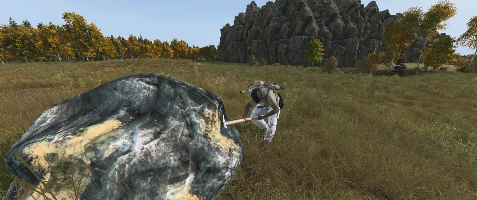A survivor swinging a pickaxe at a large ore boulder in a meadow below a rock face